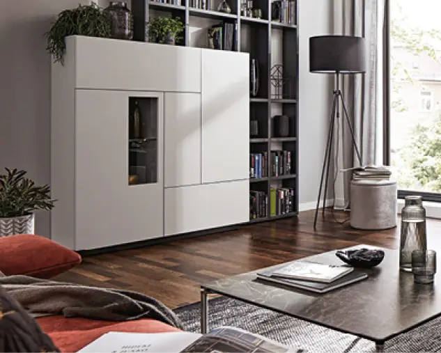 Helle Wohnwand mit geschlossenen Schränken und integriertem Bücherregal im Wohnzimmer. Zeitgemäße Möbelkombination mit viel Stauraum für Bücher und Wohnaccessoires.